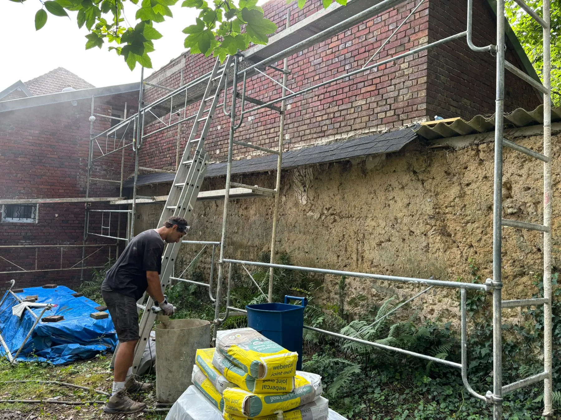 Ouvrier au pied d’un mur ancien en brique et pierre, échafaudage dressé